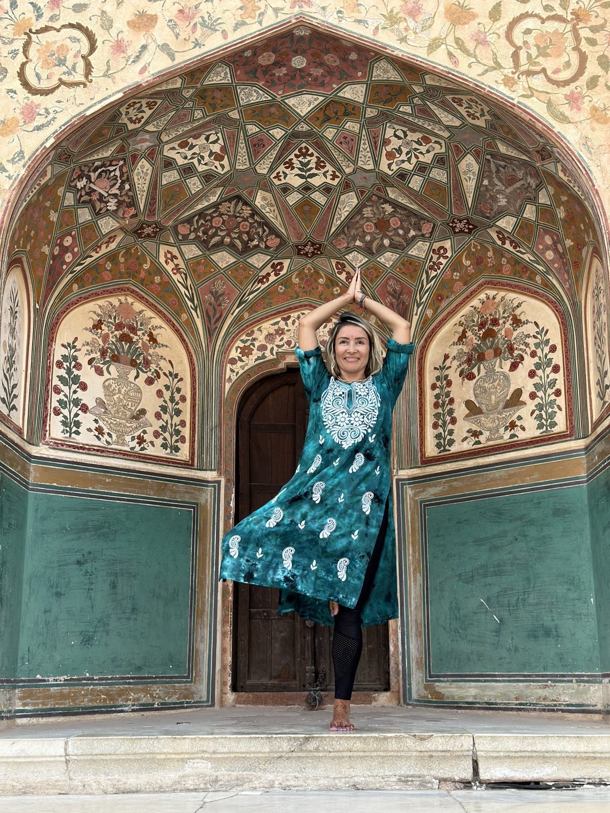 Olga en postura del árbol bajo un arco pintado de un palacio en India
