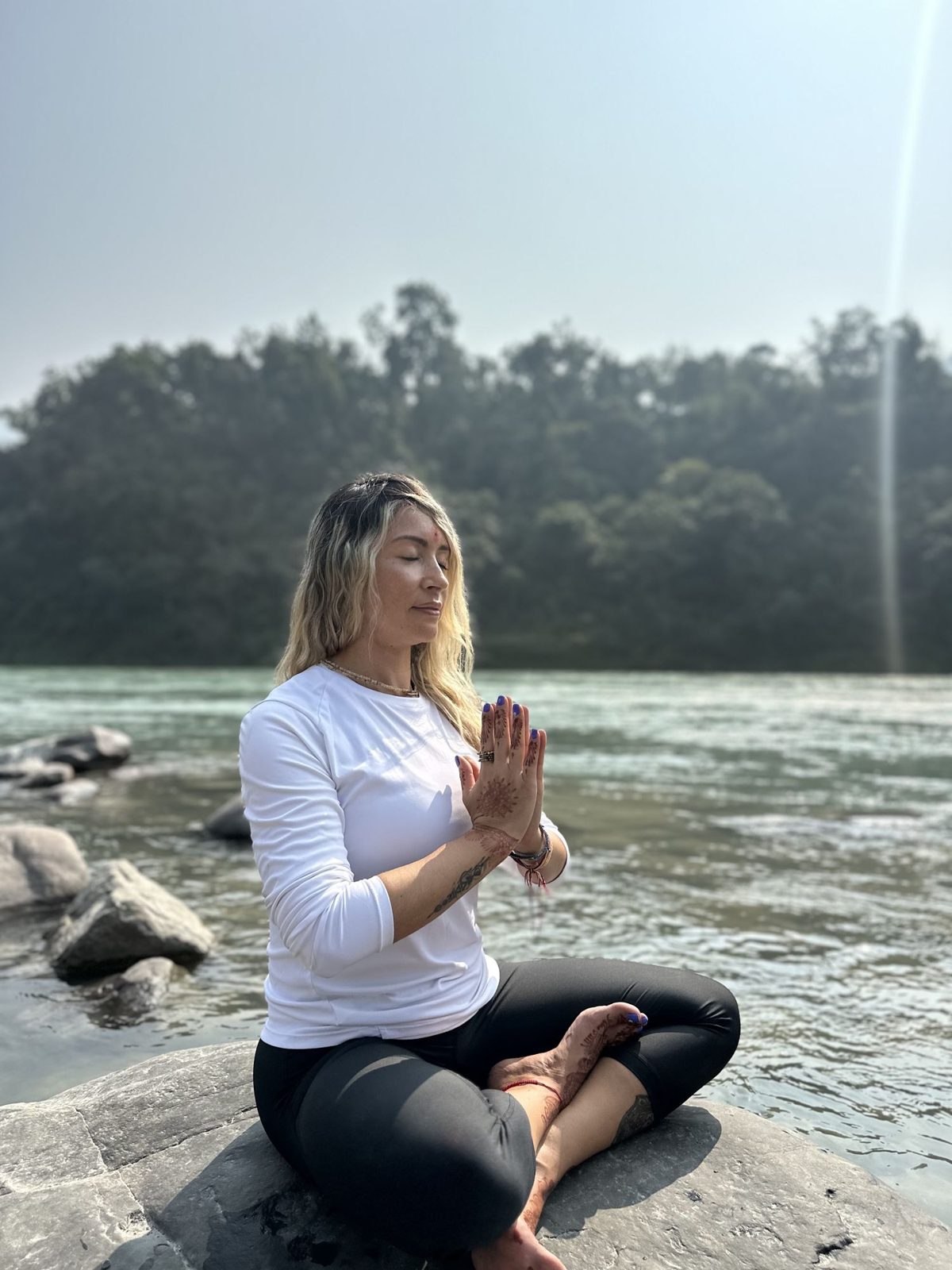 Olga meditando con las manos unidas a la orilla de un río en India
